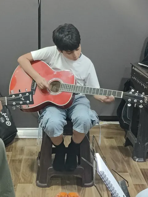 A young learner practising a red acoustic guitar at DSM Dwarka Sector 22